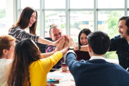 group of young multiethnic diverse people gesture hand high five, laughing and smiling together in brainstorm meeting at office, company culture