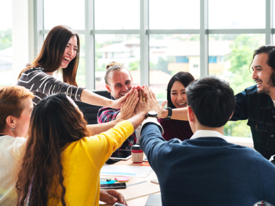 group of young multiethnic diverse people gesture hand high five, laughing and smiling together in brainstorm meeting at office, company culture