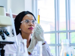 International Day of Women and Girls in Science, African female scientist in protective glasses looking and testing tube chemical in laboratory, development for the future.