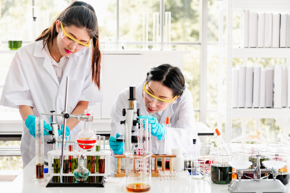 Young asian female chemists with senior caucasian chemist working together in lab, looking into microscope, Women in STEM
