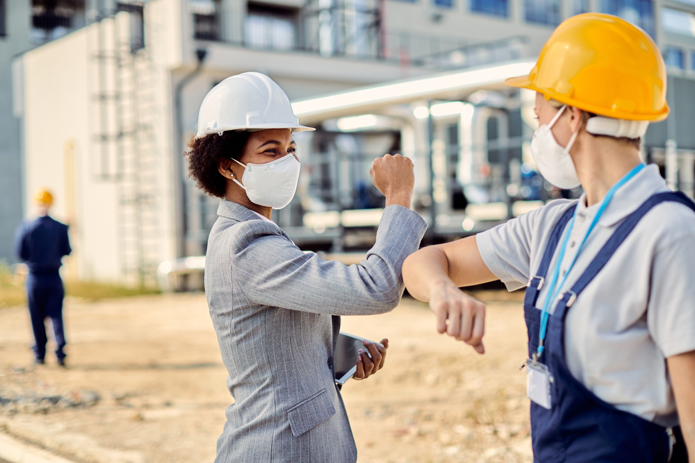 Happy African American building contractor and construction worker greeting with elbows during coronavirus epidemic, women in STEM, women in engineering