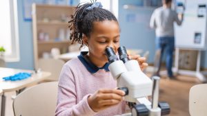 Portrait of Smart Little Schoolgirl Looking Under the Microscope. In Elementary School Classroom Cute Girl Uses Microscope.jpg