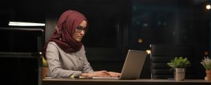 Young Muslim woman wearing a Hijab, working late at night on a computer