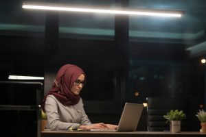 Young Muslim woman wearing a Hijab, working late at night on a computer