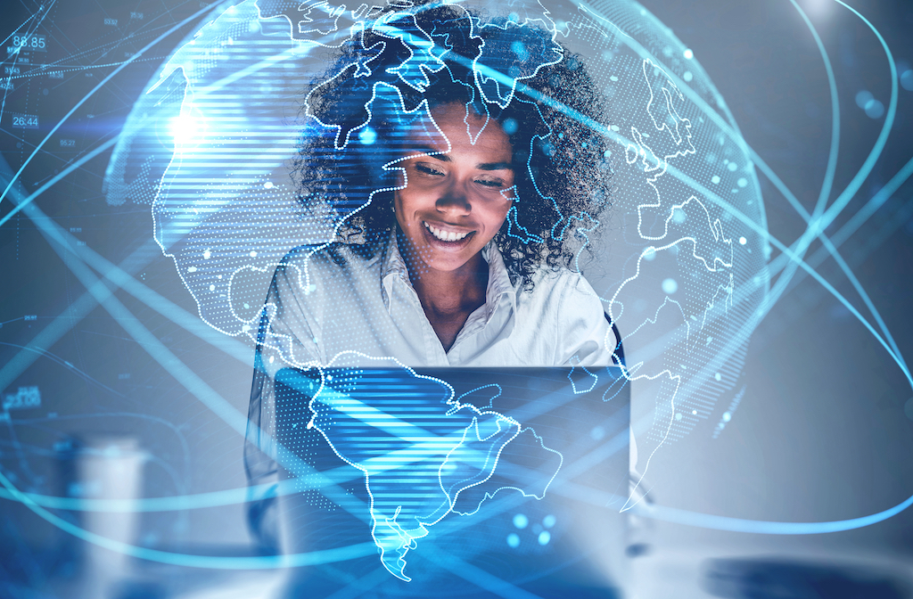 Cheerful young African American woman using laptop in blurry office with double exposure of futuristic network interface and planet hologram. Concept of internet and communication. Toned image, woman in tech