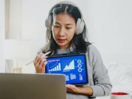 Asian businesswoman wearing headphones, analysing data working from home