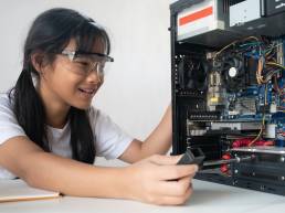 Young woman fixing computer at white table, girls in stem