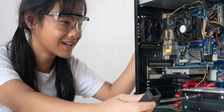 Young woman fixing computer at white table, girls in stem