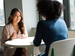 Two women of diverse backgrounds talk at a business meeting