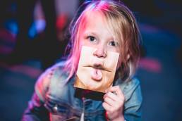 Child holding up part of a mask obscuring their mouth with a printed image of a mouth